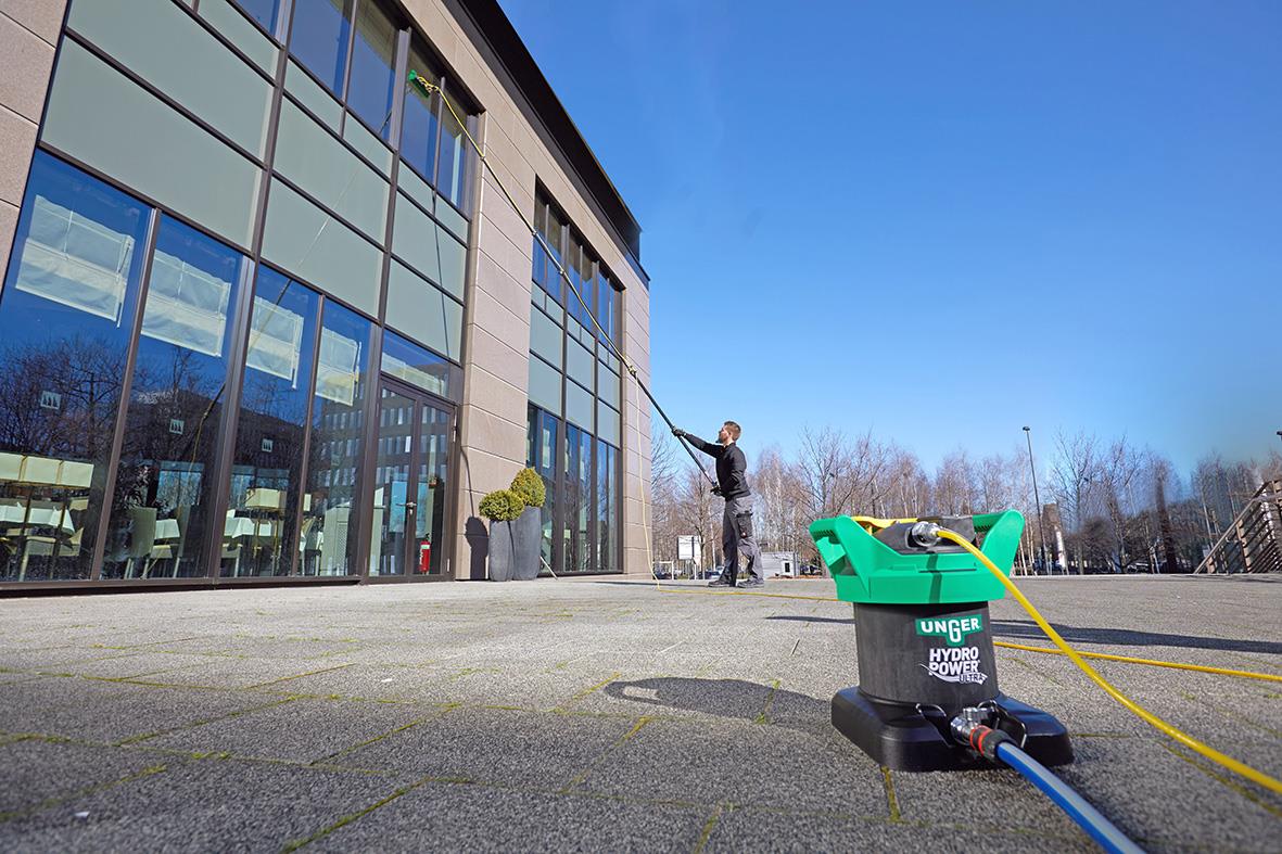 Person rengör fönster med Unger HydroPower Ultra Carbon 6m på en modern byggnad
