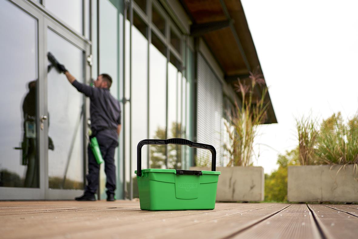 Person som rengör stora fönster utomhus med fönsterputsutrustning och en grön förvaringskorg