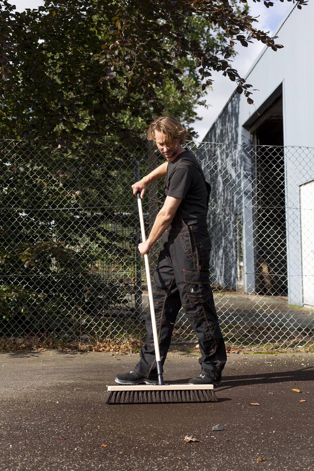 Person med träskaft Vikan Gängad 155cm sopar utomhus framför stängsel och byggnad