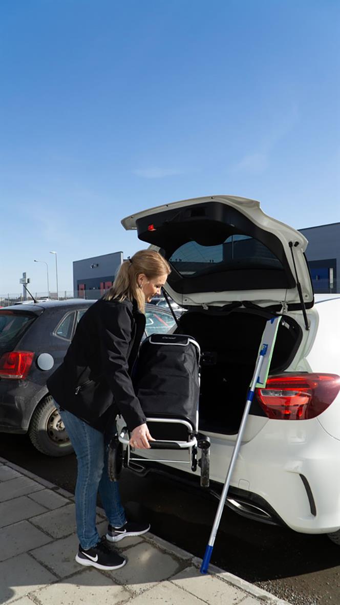 Kvinna packar en städvagn i bakluckan på en vit bil på parkeringsplats under klar himmel