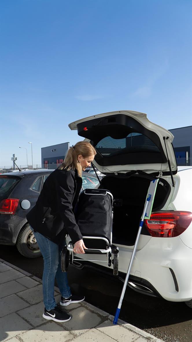 Kvinna lastar en städvagn i en bils bagageutrymme på en parkeringsplats