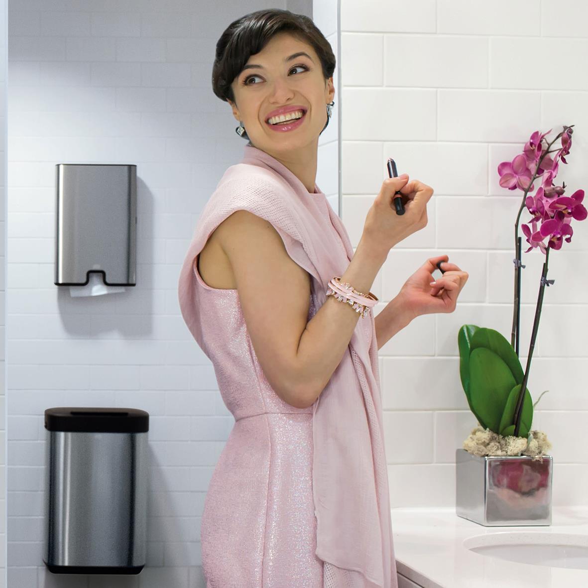 Glad kvinna i rosa klänning skriver på en whiteboard i ett kontorsutrymme med växt och papperskorg