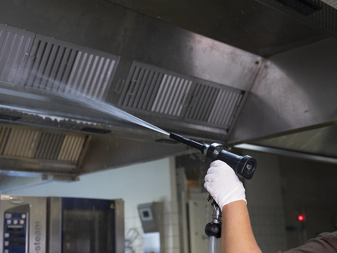 Person rengör ett munstycke med högtrycksslang under köksfläkt