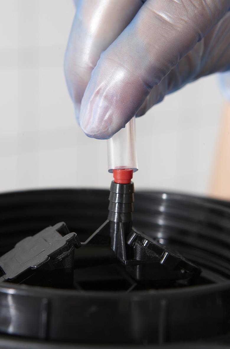 Hand som håller en injektor med svart sugslang över en svart behållare