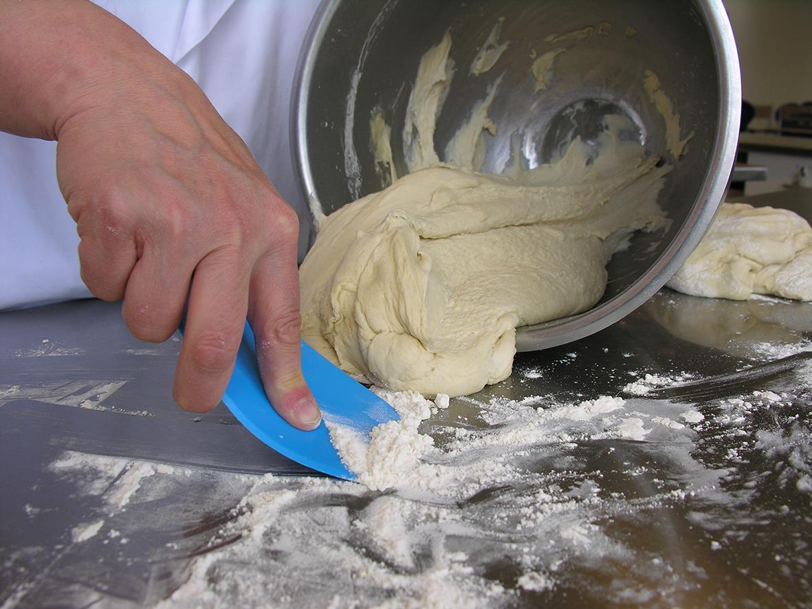 Person använder en grön Vikan flexibelskrapa för att skrapa deg från ett arbetsbord