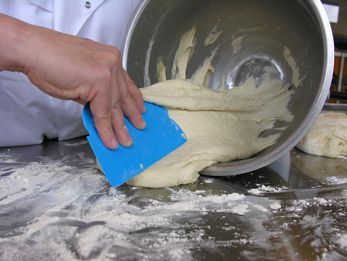 Person använder en grön Vikan flexibelskrapa för att skrapa deg från en arbetsbänk