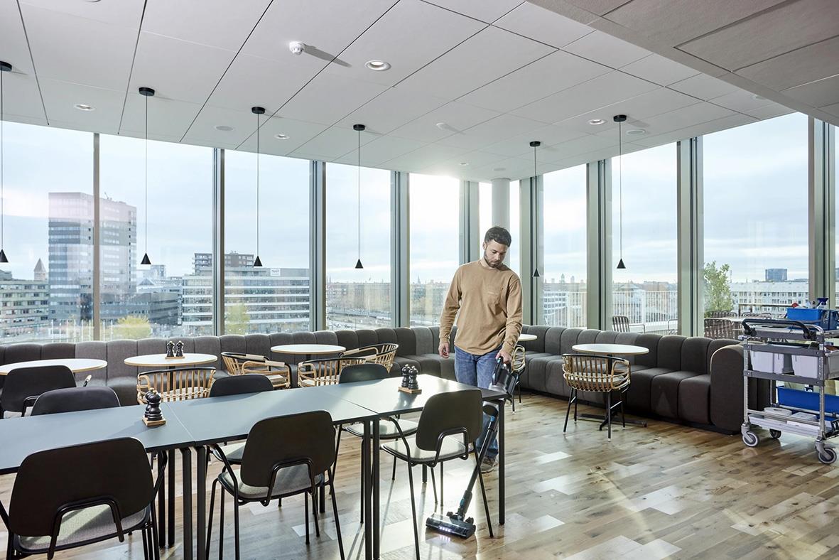 Person städar i ett stort konferensrum med stora fönster och stadssilhuett i bakgrunden