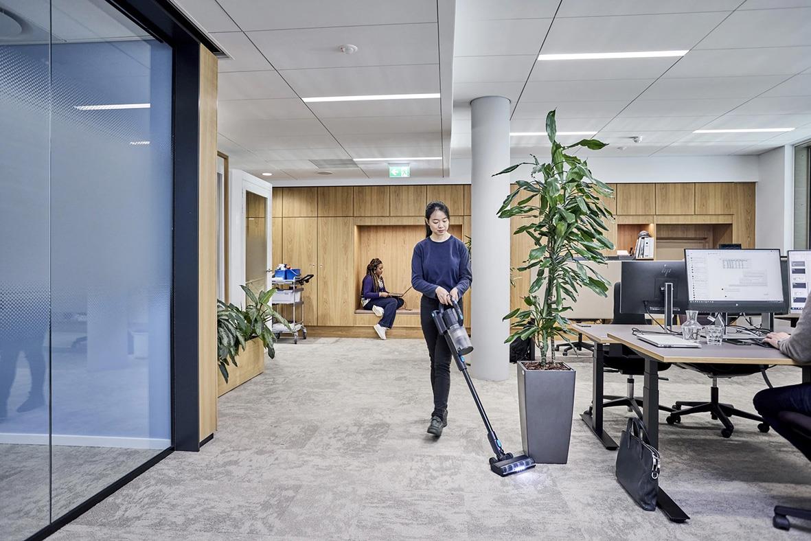 Person som dammsuger kontorsgolv med Nilfisk VU200 dammsugare i ett kontorslandskap