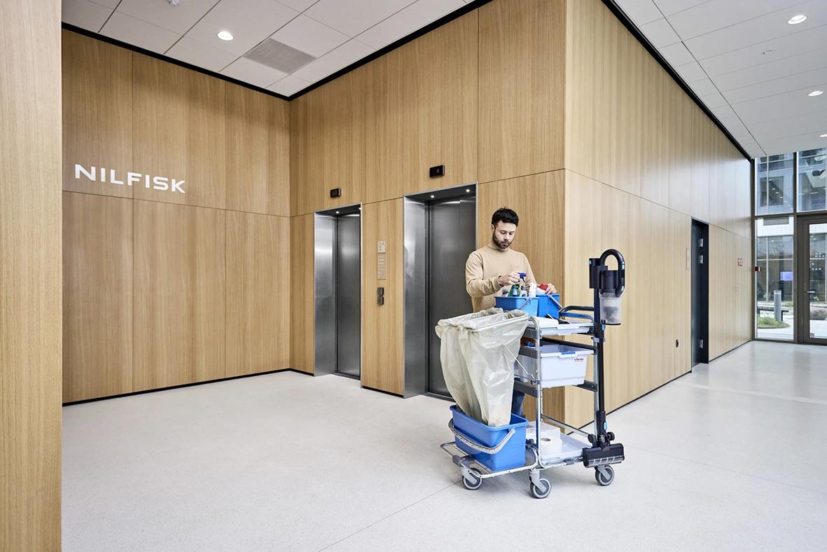 " med vagn med tvätt i ett modernt, trägolv och väggmiljö nära hissar i ett byggnadskorridor"