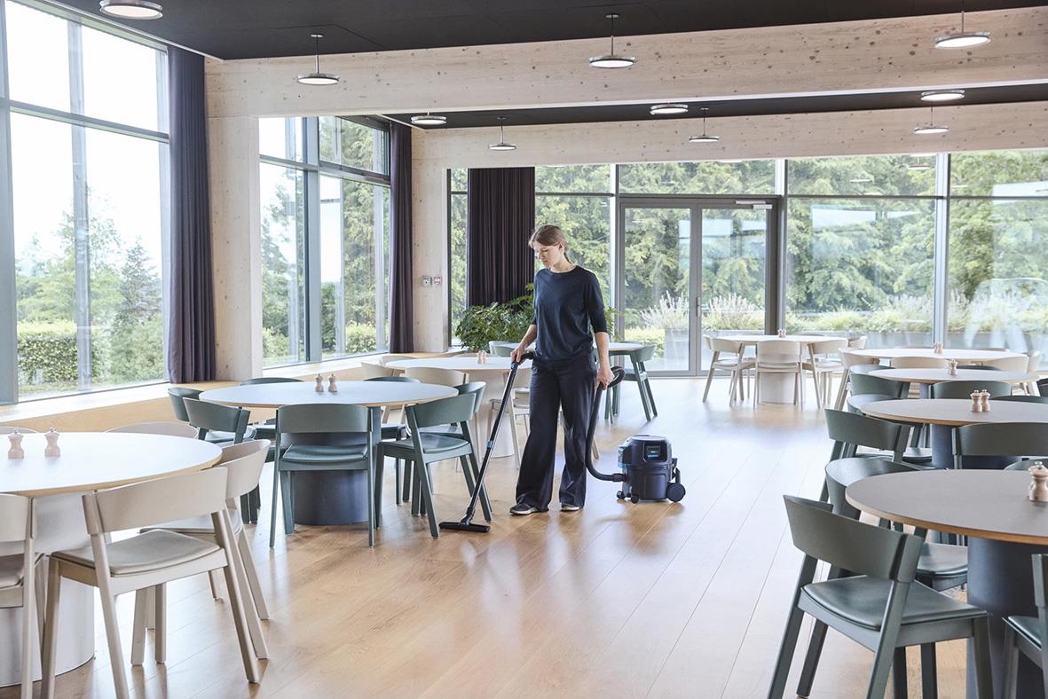 Person städar i ett modernt, tomt konferensrum med stora fönster och trämöbler