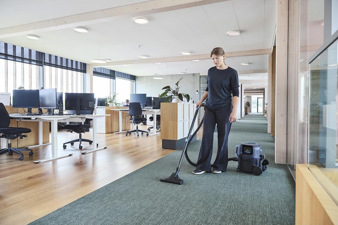 Person städar med Nilfisk VP500 R H BP+ EU/UK batteridriven dammsugare i kontorsmiljö