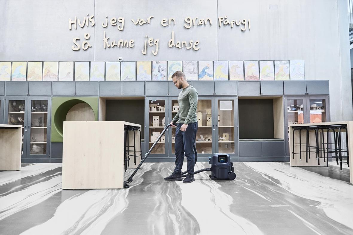 Man använder en Nilfisk VP500 R H BP+ EU/UK batteridriven dammsugare i ett modernt inomhusmiljö