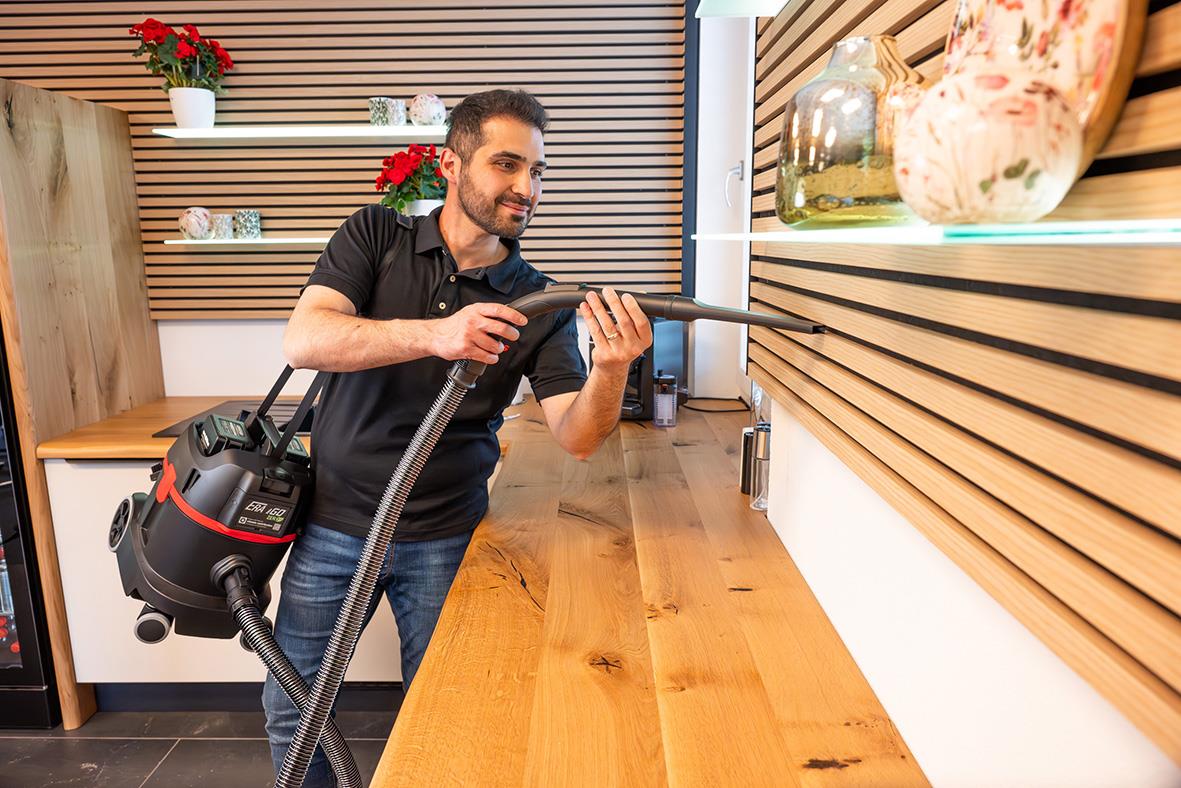 Man använder en batteridriven dammsugare Sprintus ERA IGO ZERO på en träbänk i ett modernt hem.