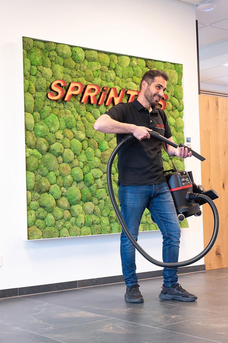 Man med dammsugare framför en vägg med gröna mossa och SPRINTERS i rött text