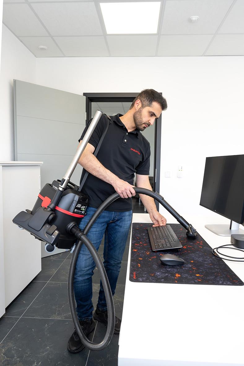 Man använder dammsugare Sprintus ERA IGO ZERO batteridriven 2x18V 5Ah på ett skrivbord i ett kontorsrum