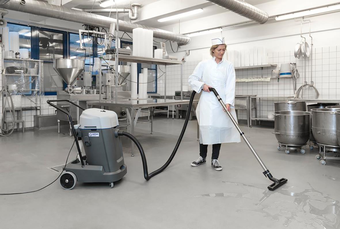 Person använder en Nilfisk VL500 55-2 Ergo våt- och torrsug i ett industriellt kök eller laboratorium