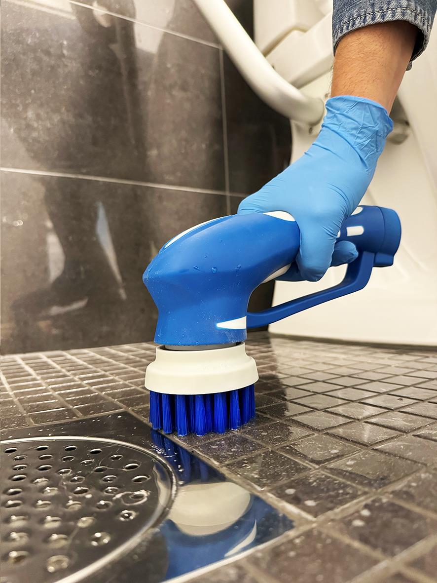 Person använder Skurmaskin Activa Handy Scrubber med blå handskar för att rengöra badrumsgolv.