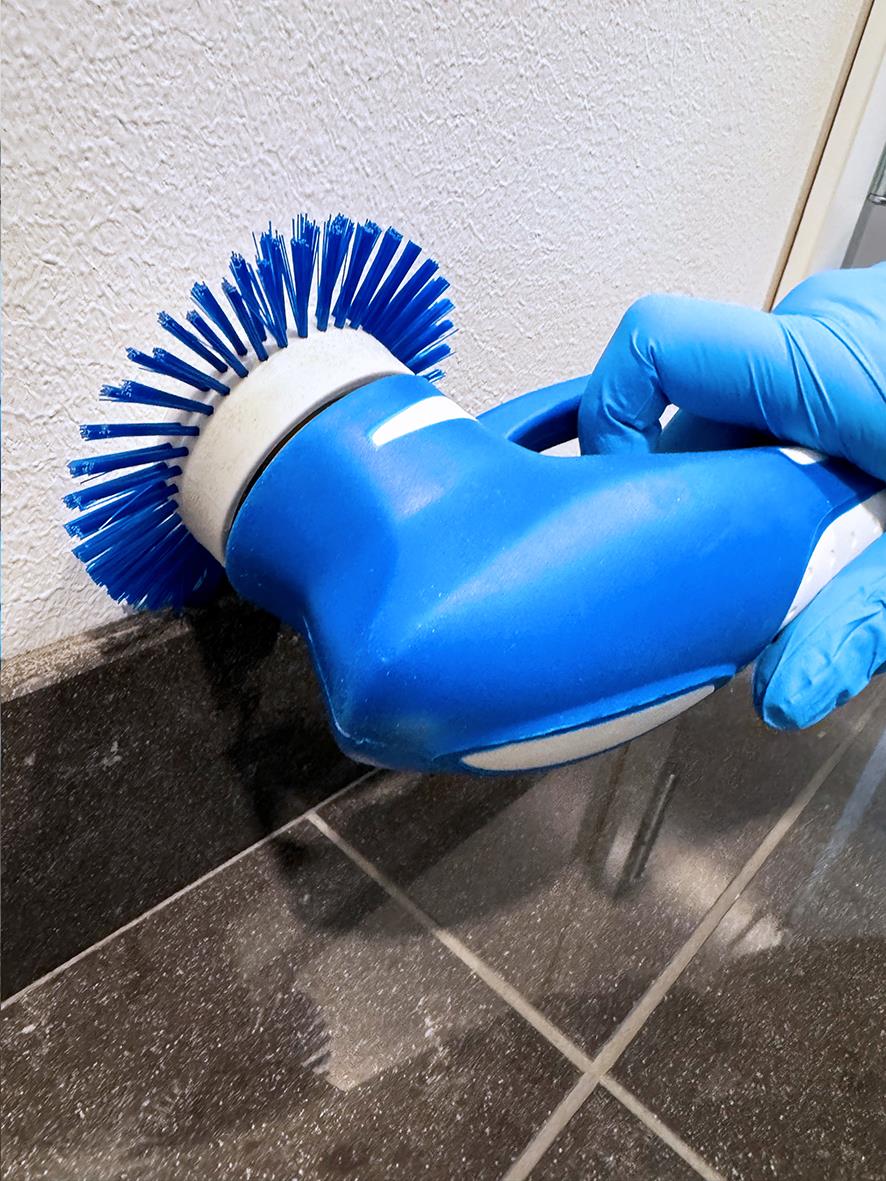 Handskyddad person använder en blå skurmaskin för att rengöra golvet