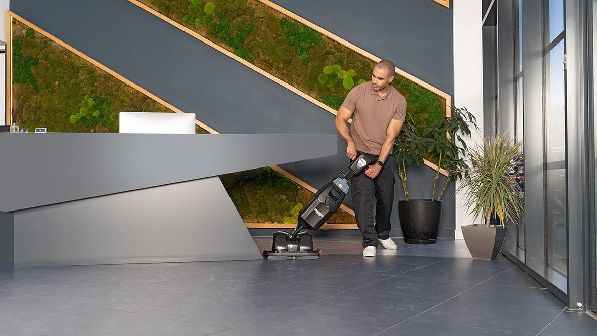 Person använder en kombiskurmaskin Nu-Mop Flex 2.2I med batteri i ett modernt inomhusmiljö