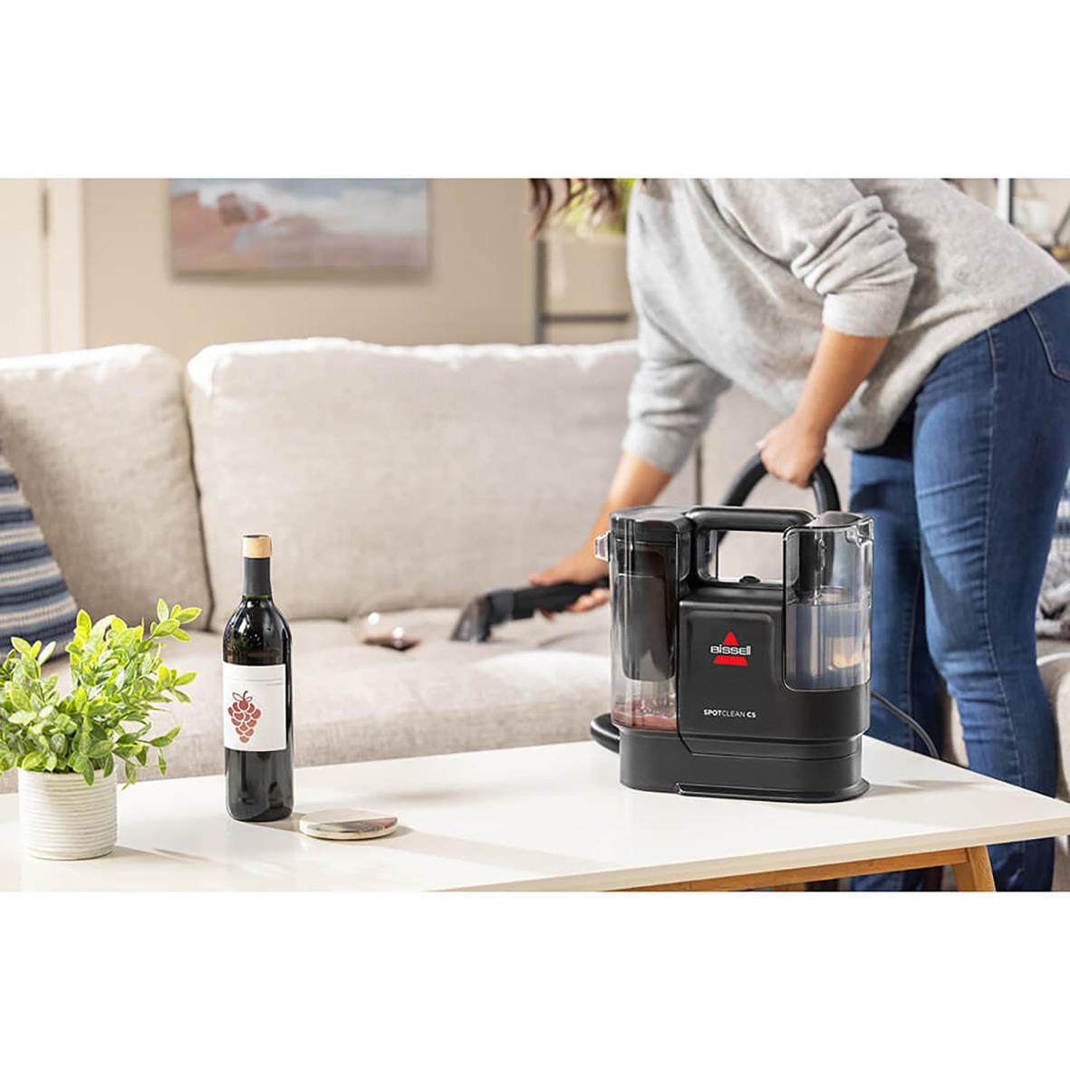 Person som rengör en soffa med Bissell Spotclean C Pro, en rengöringsmaskin på ett bord