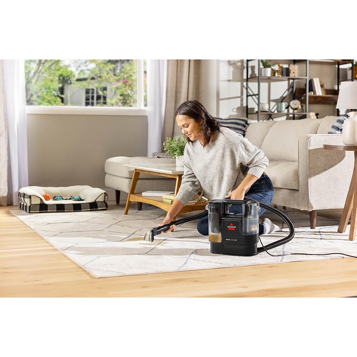 Kvinna använder Bissell Spotclean C Pro för att rengöra matta i vardagsrum med soffa och fönster i bakgrunden