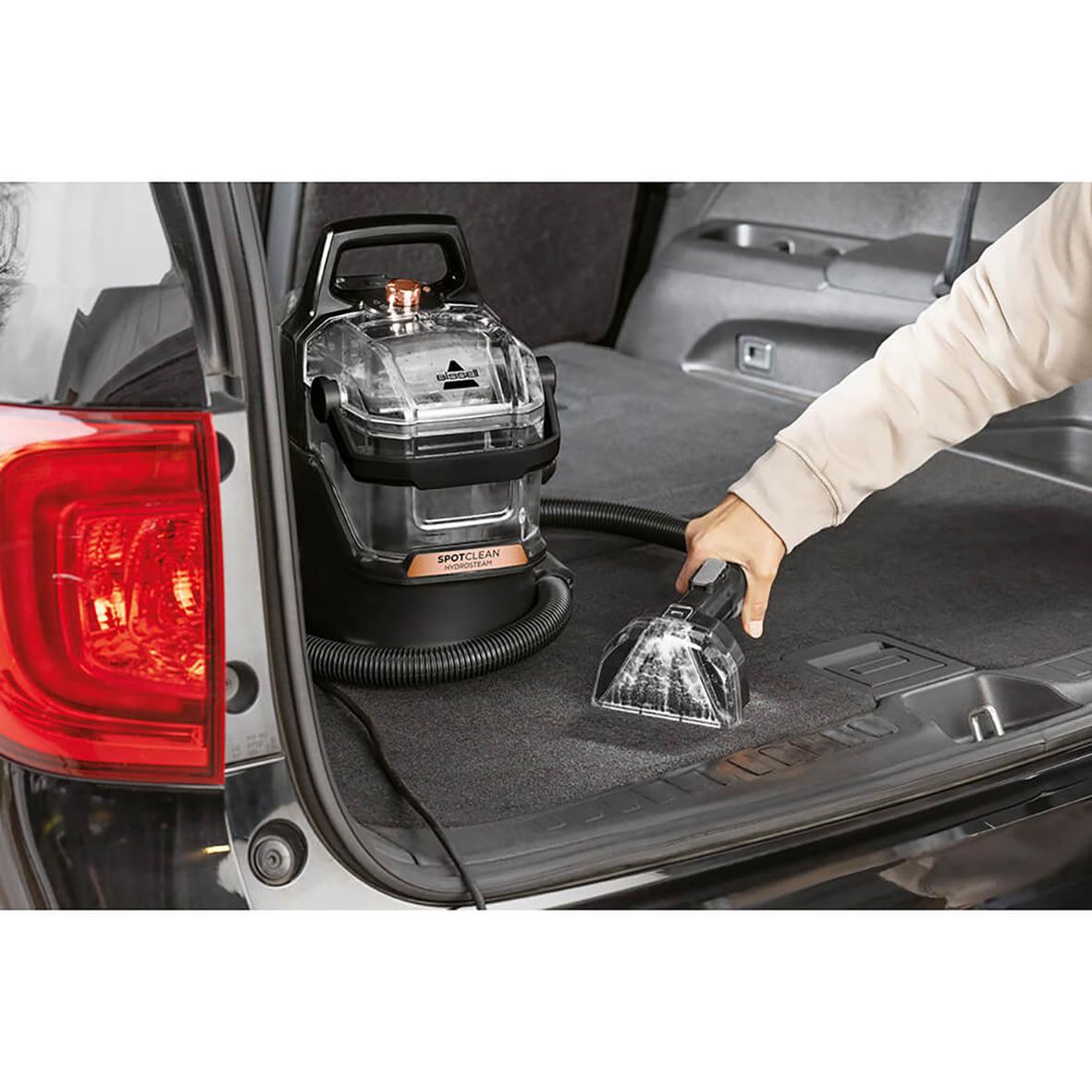 Person använder Bissell Spotclean Hydrosteam Pro för mattvätt i bilens bagageutrymme