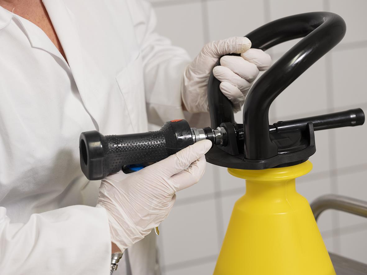 Person som fyller en grön skumspruta med stålrör i ett laboratorium eller industriell miljö