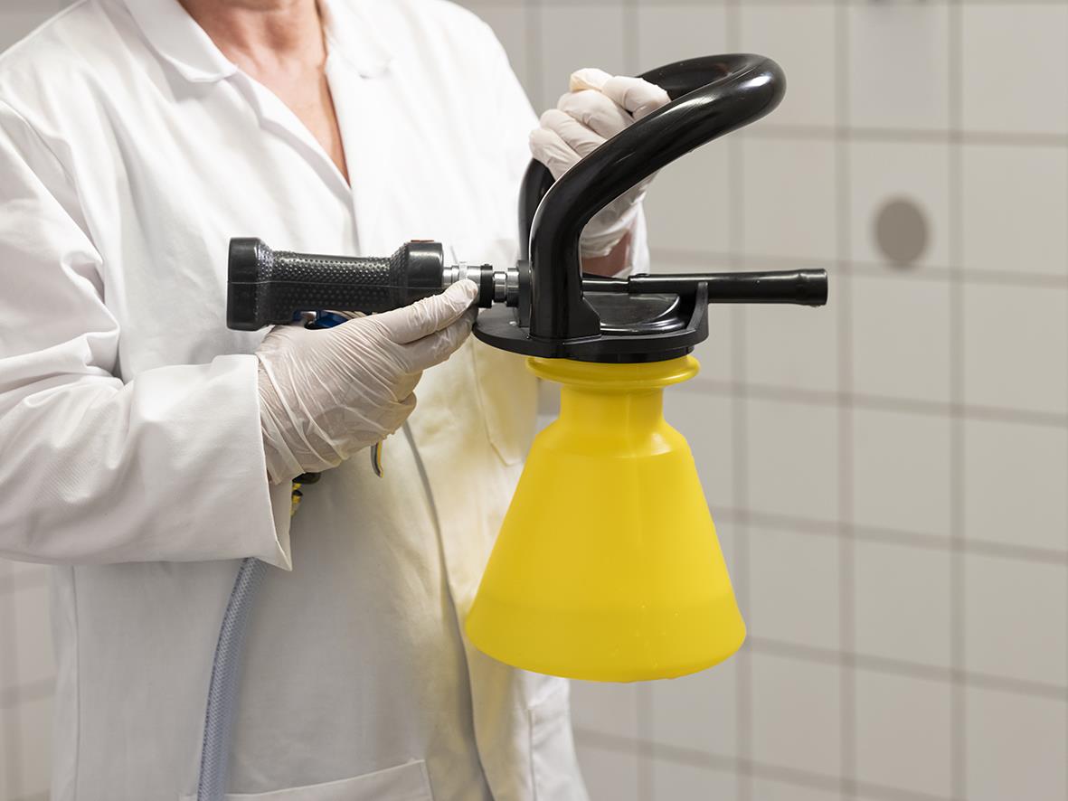 Person i vit labbrock använder skumspruta Vikan med stålrör och grön behållare på klinik eller laboratorium