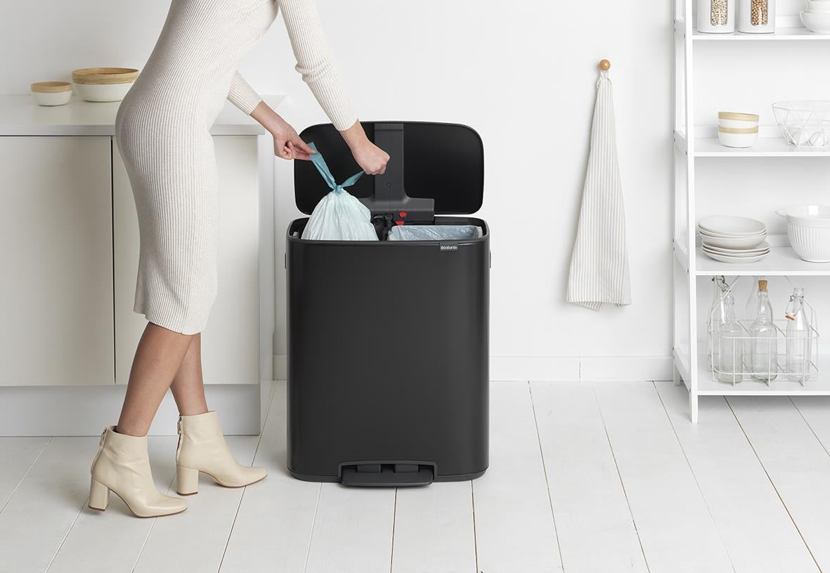 Person som slänger en svart Brabantia Bo Matt pedalhink med 2x30L kapacitet i ett vitt kök