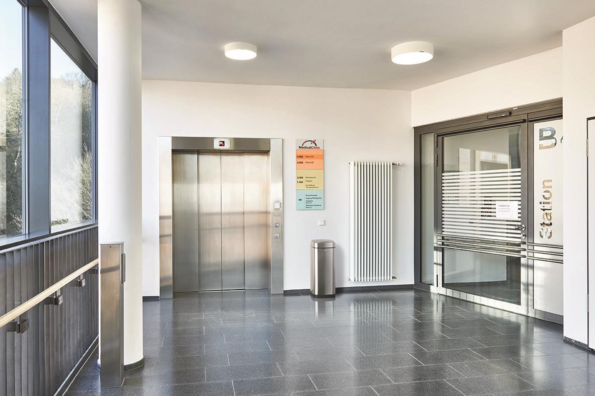 Silver papperskorg med touchsensor i ett modernt inomhusmiljö nära hiss och entré