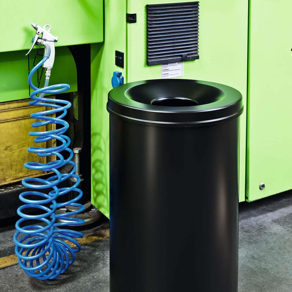 Svart papperskorg Durable Safe 60L placerad framför gröna maskiner och en blå slang