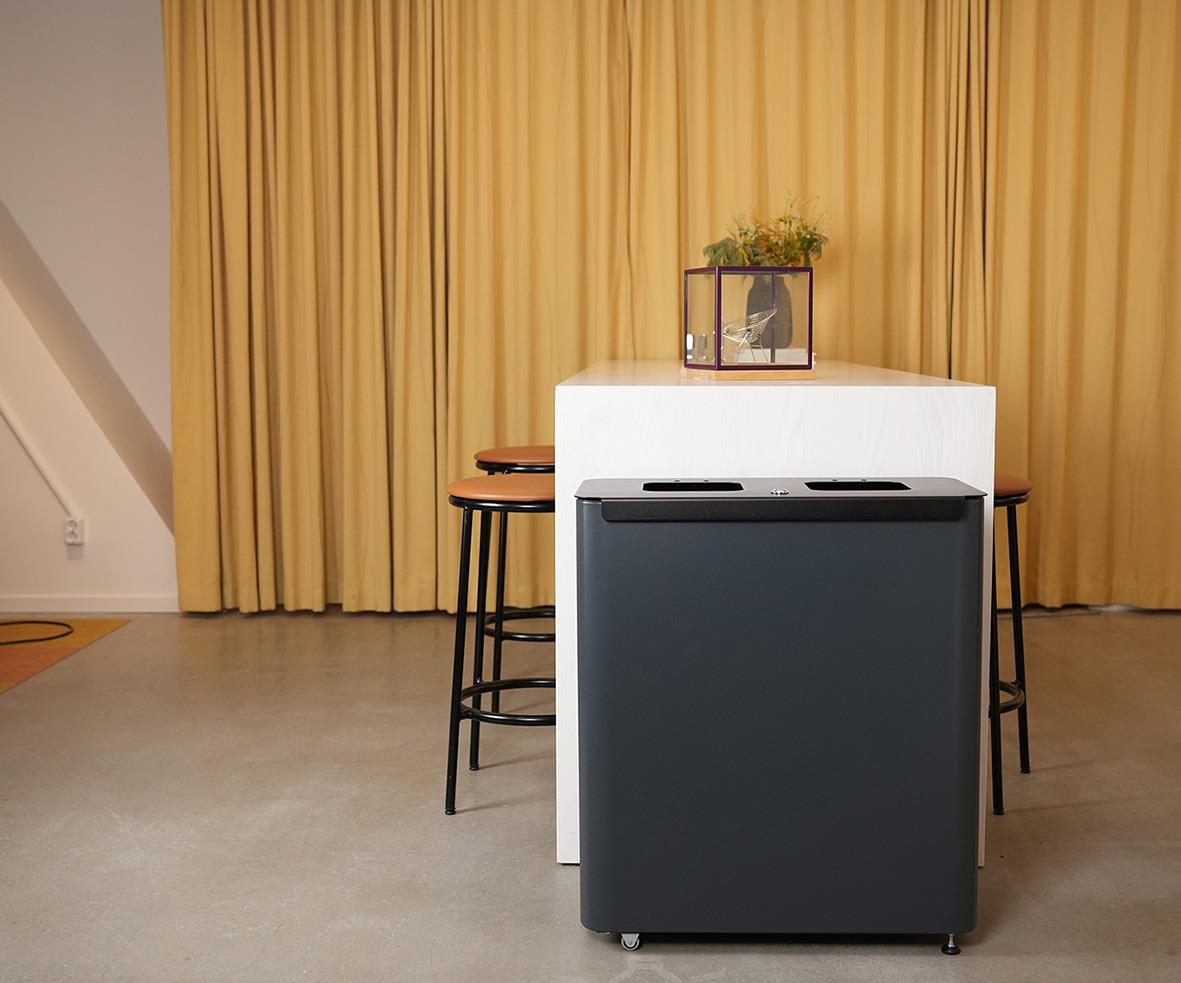 Sorteringskärl Star Station 2x60l i grå/svart framför en gul gardin