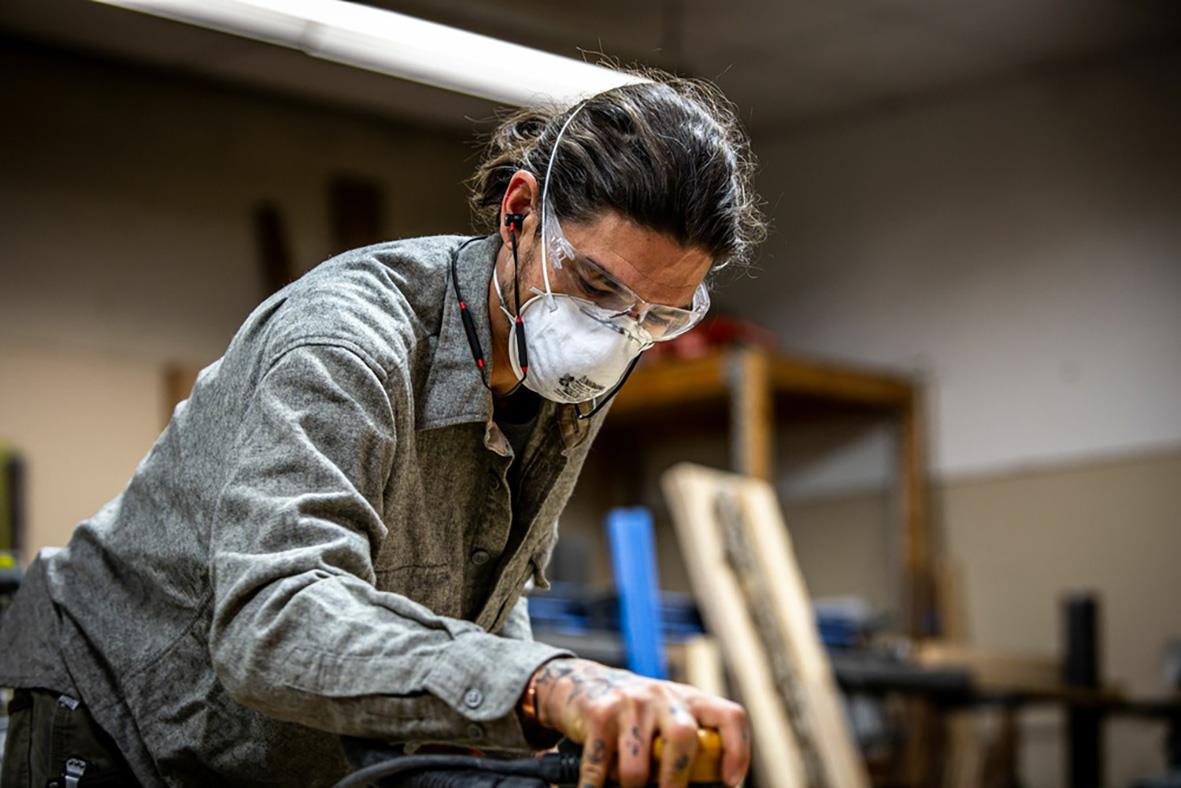 Person med hörselproppar och ansiktsmask arbetar i verkstad