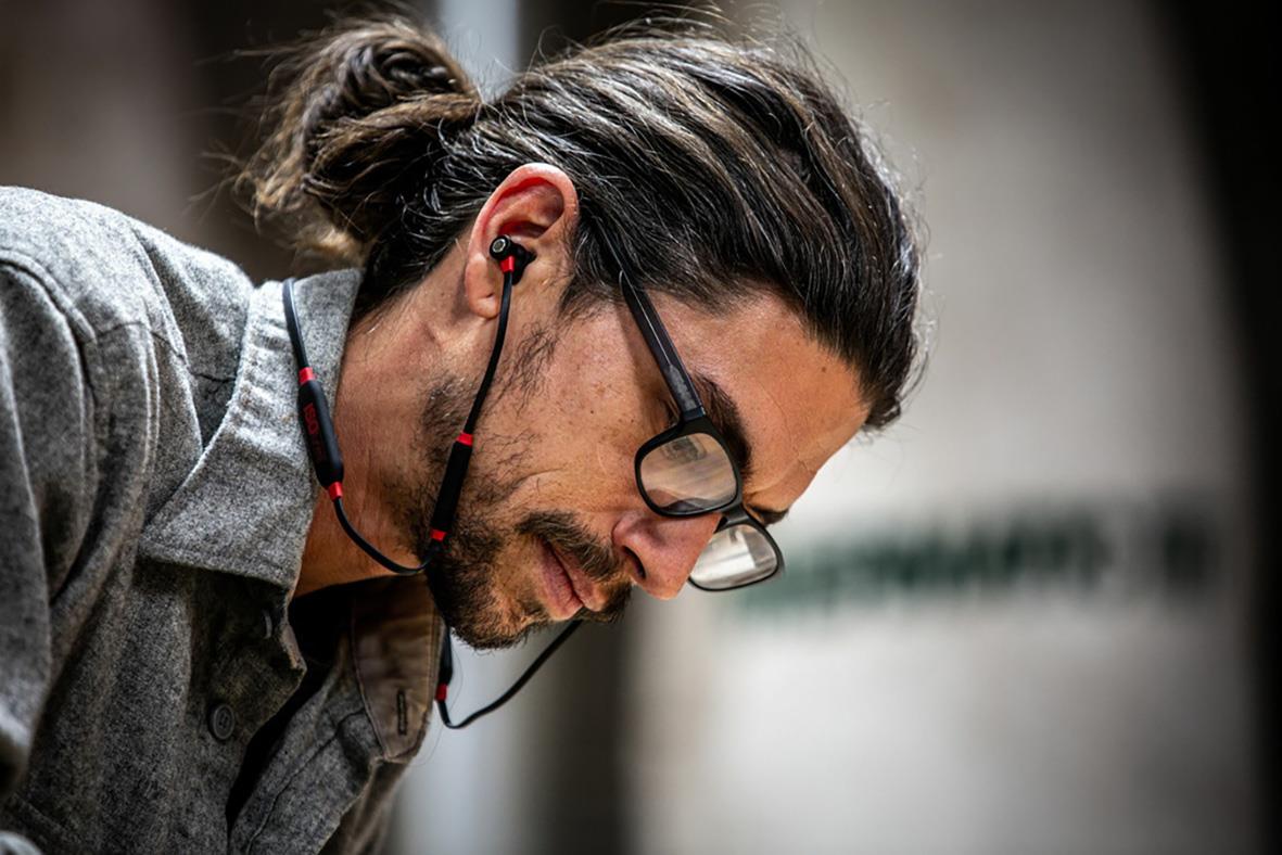 Man med långt hår, glasögon och hörselproppar som lyssnar på musik eller ljud