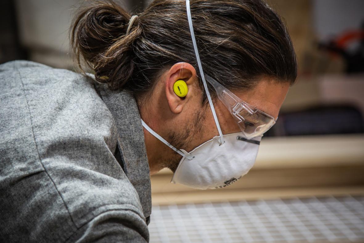 Person med skyddsglasögon, ansiktsmask och hörselproppar som arbetar i en verkstad eller industriell miljö