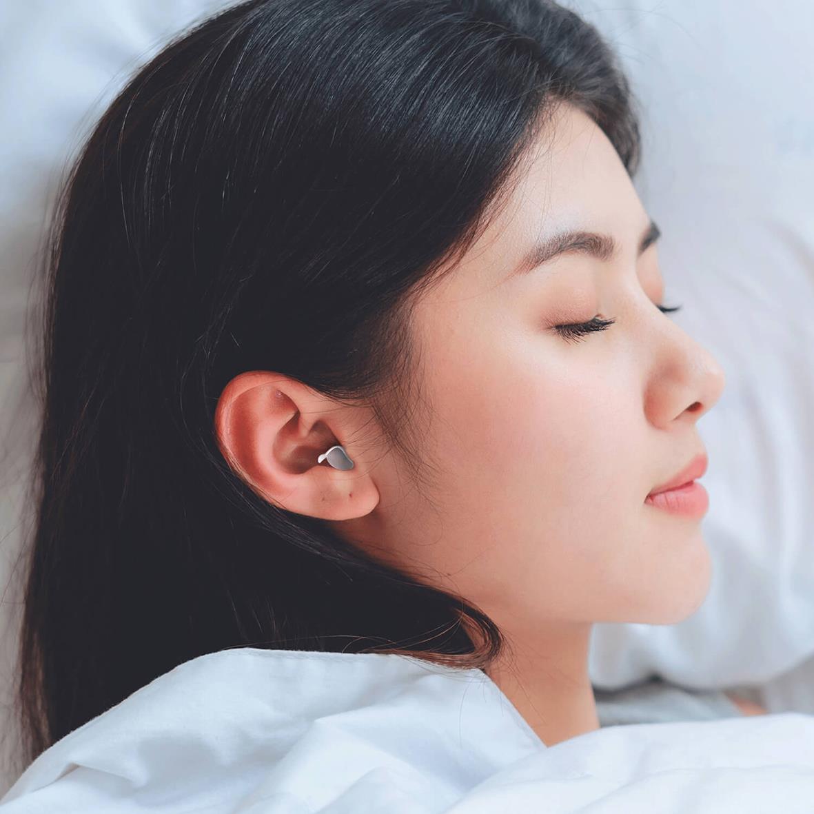 Kvinna med hörselskydd som sover på sidan i säng