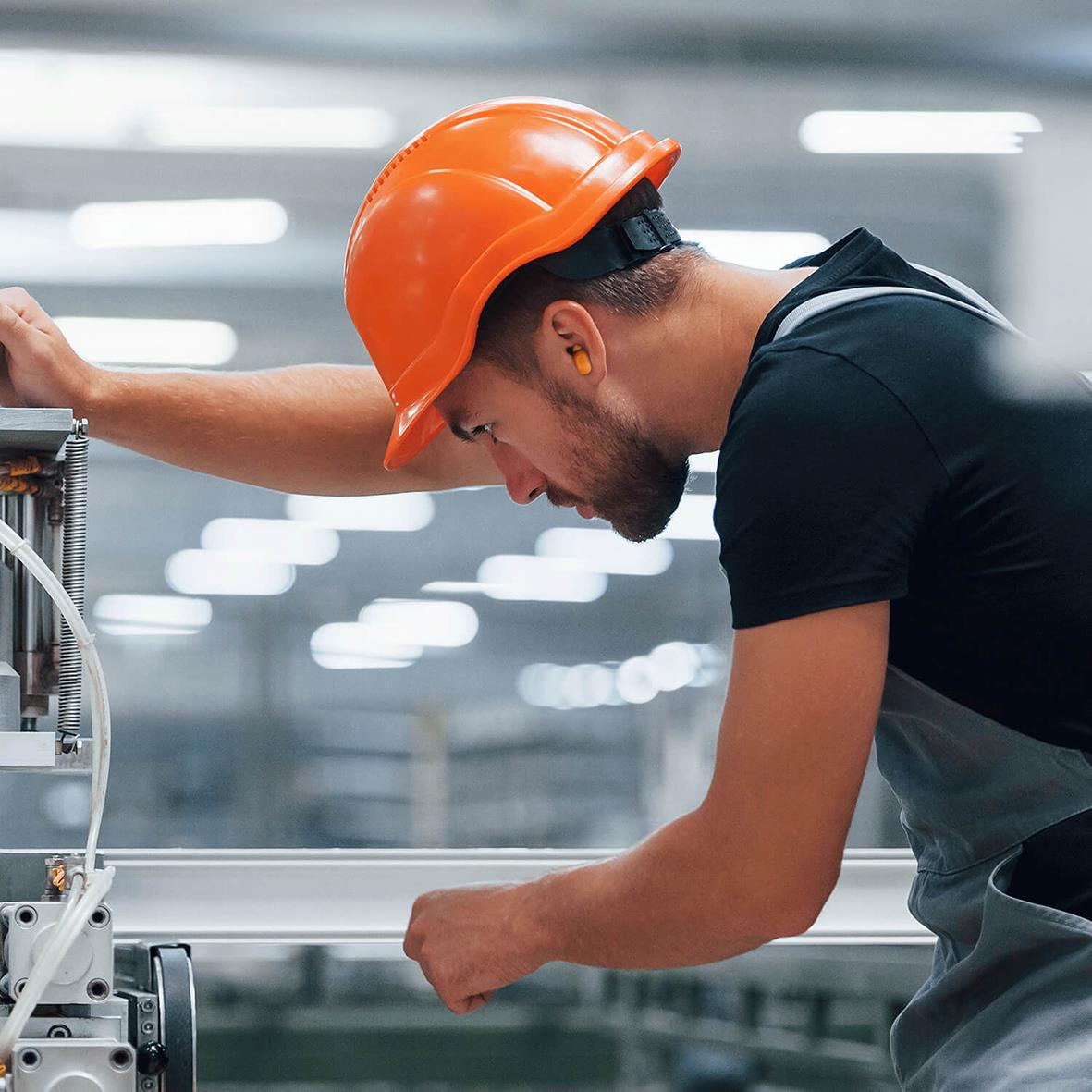 Arbetare i industrimiljö med orange hörselskydd och hjälm, arbetar med maskiner