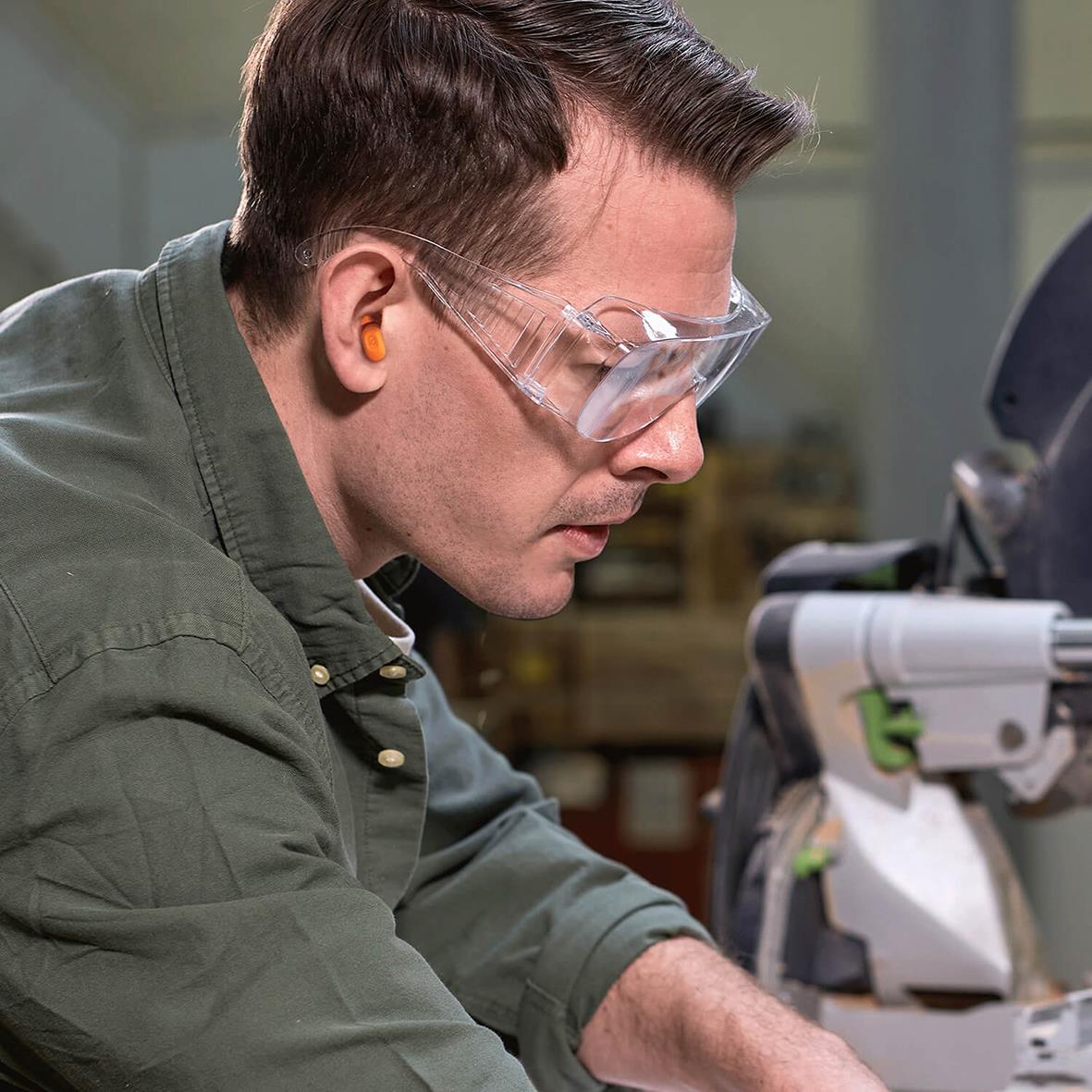 Man med hörselskydd och skyddsglasögon arbetar i verkstad eller labbmiljö