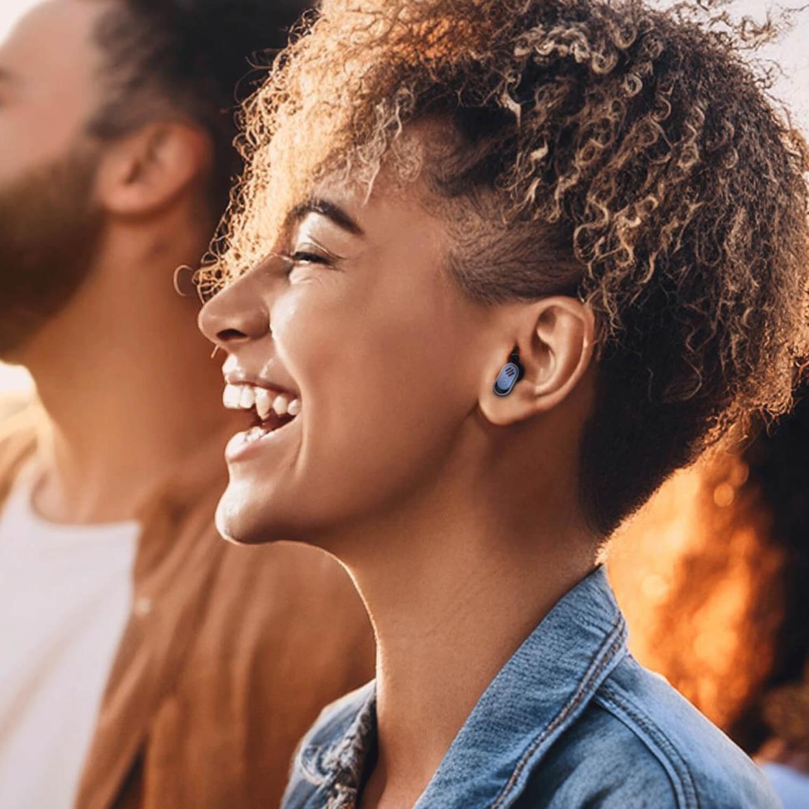 Glad kvinna med hörlurar som använder öronproppar i ett utomhusmiljö, solnedgång i bakgrunden