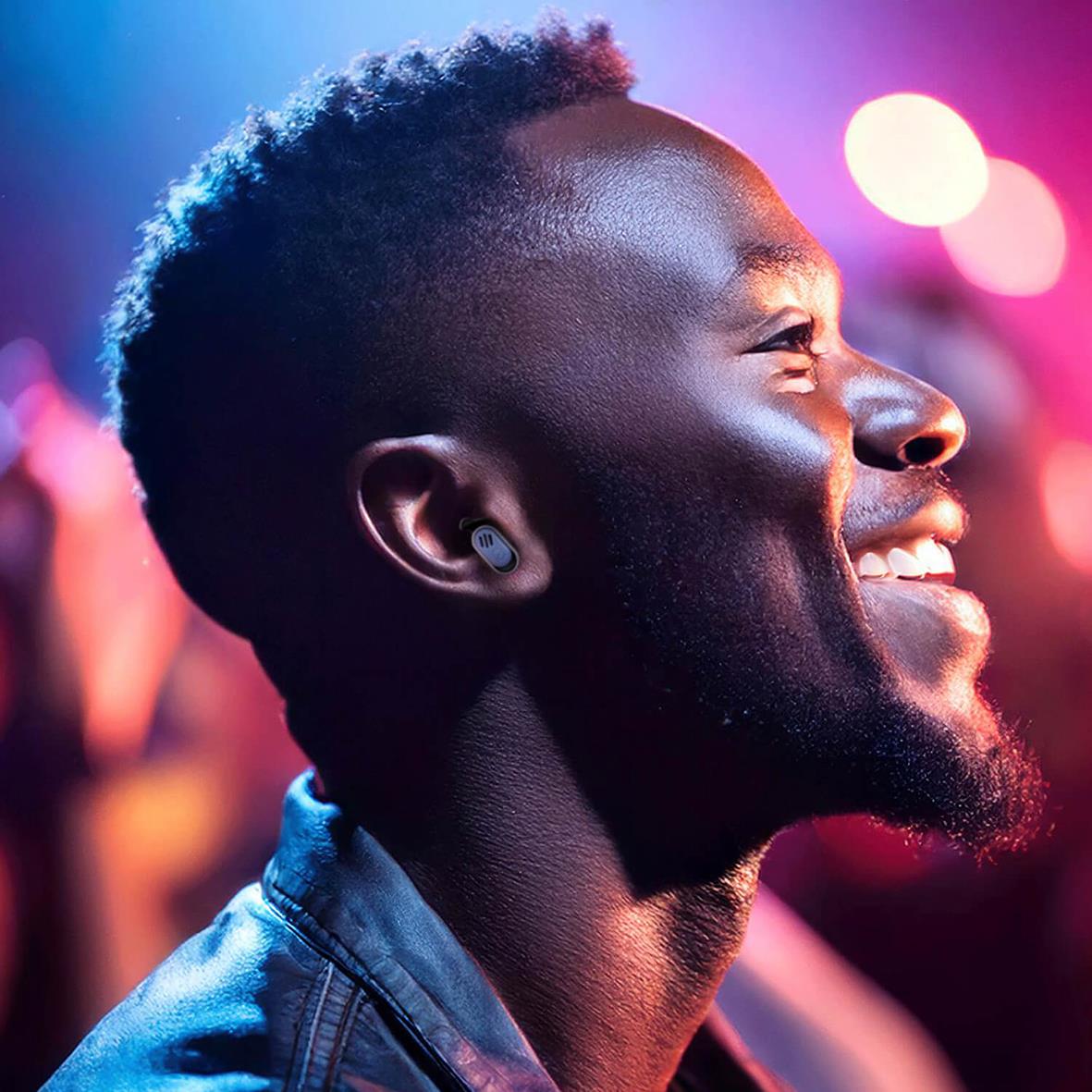 Ung man med öronproppar som lyssnar på musik på en konsert med färgglada ljus i bakgrunden