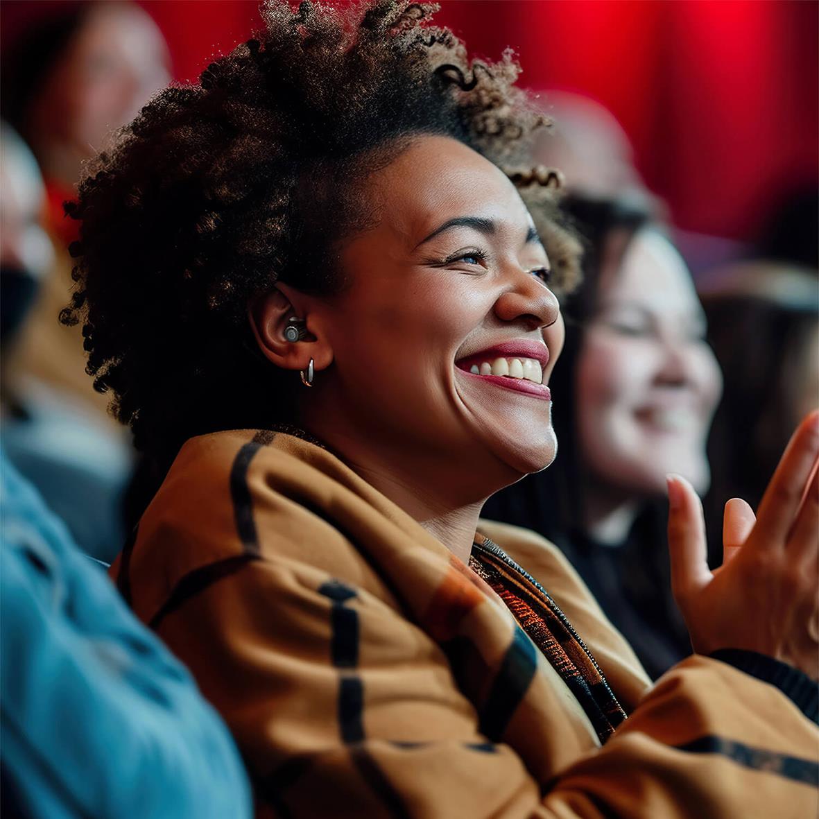 Kvinna med hörselskydd som ler och tittar framåt i en publikmiljö
