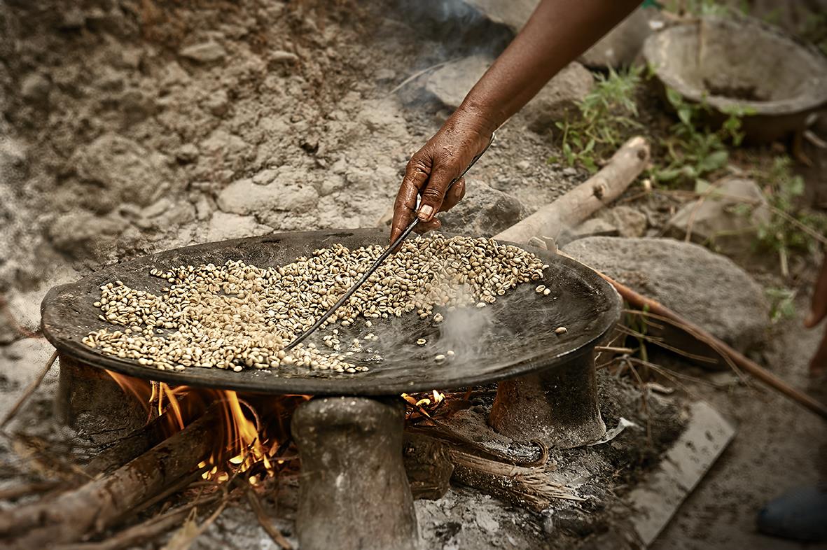 Person rostar kaffebönor i en stor panna över öppen eld