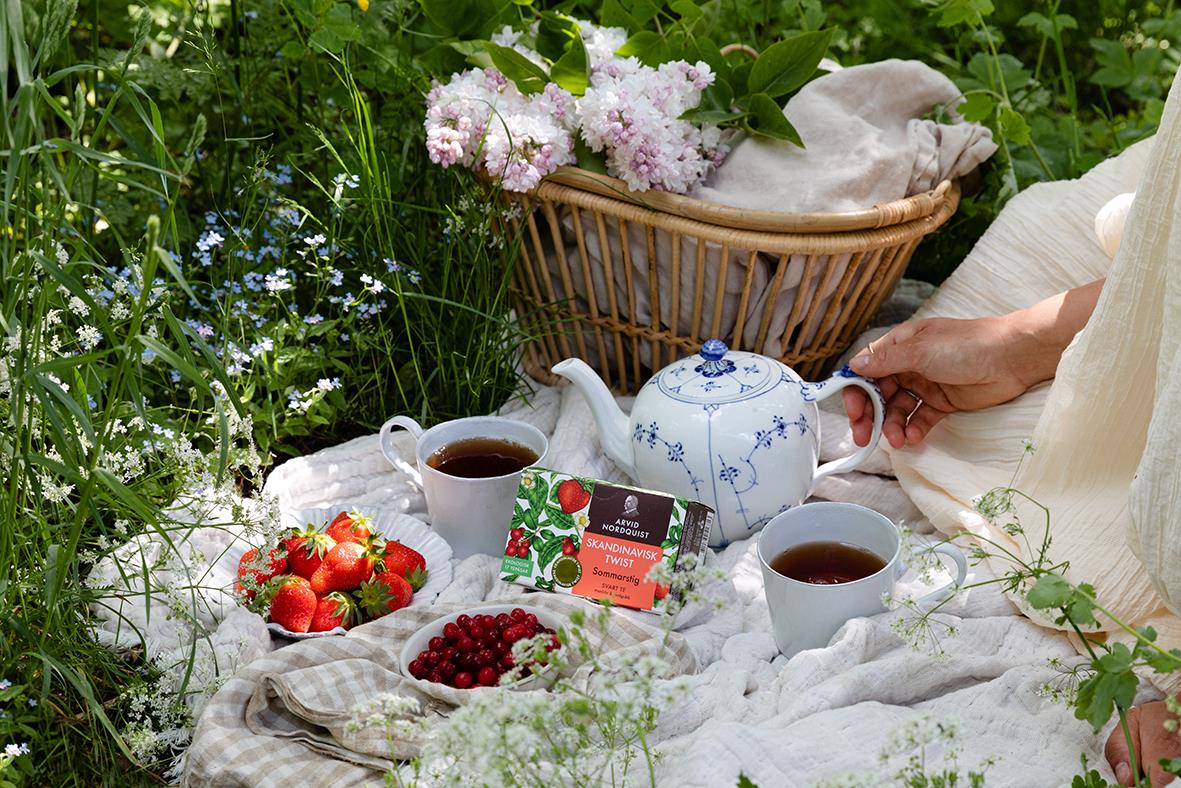 Sommarpicknick med te, jordgubbar och blommor i grönt gräs