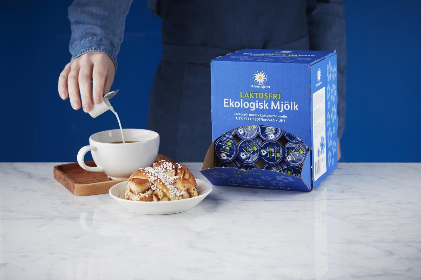 Person häller ekologisk laktosfri mjölk i en kopp på köksbänk med mjölkförpackning i bakgrunden