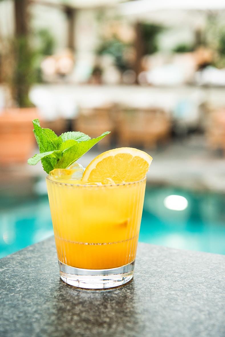 Drinkglas med orangejuice, citron och mynta på en utomhusbord, bakgrund av pool och trädgård