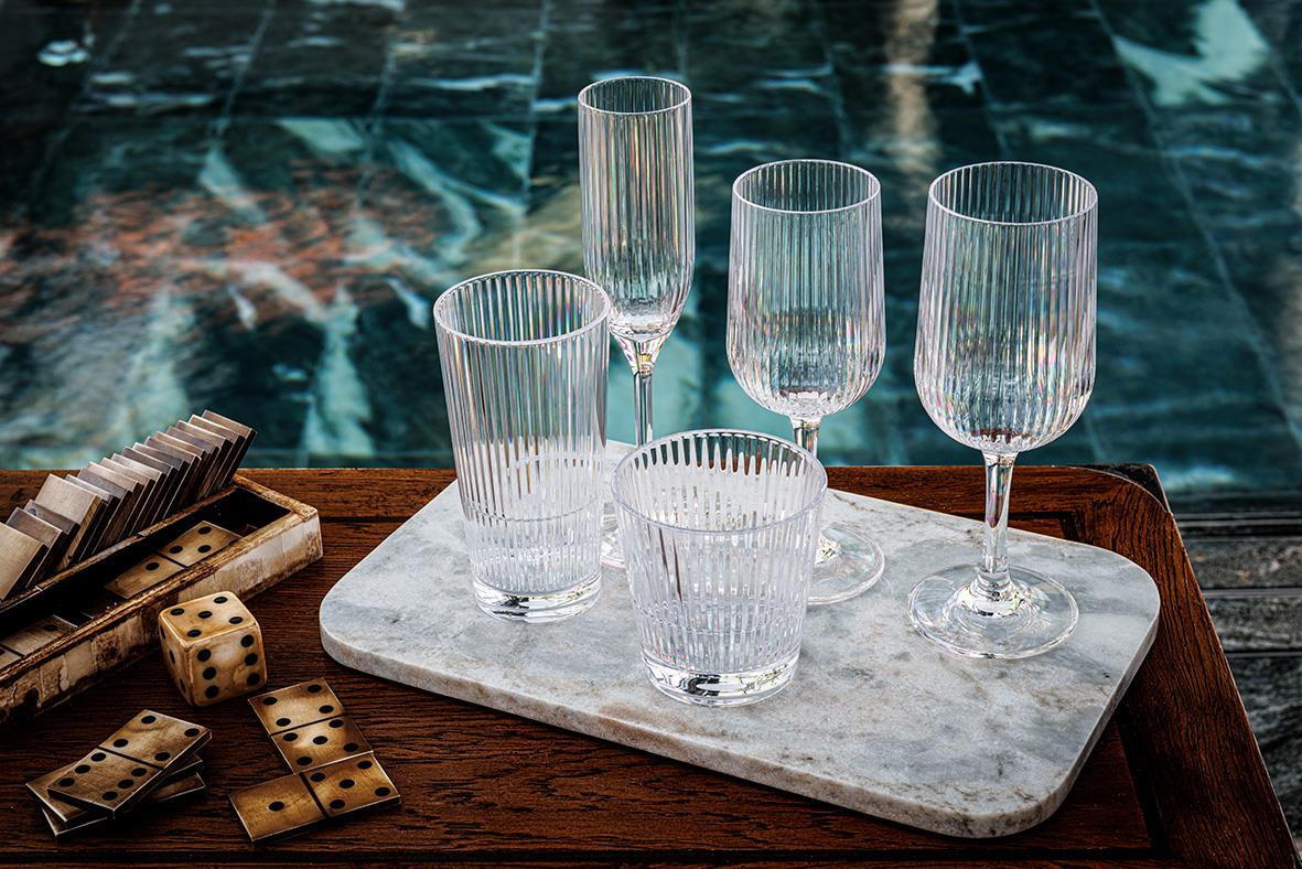 Fem drinkglas av Tritan med vertikala ränder på en marmorbård, omgivna av tärningar och en träbricka