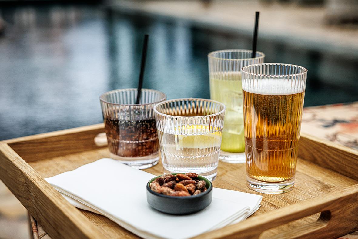 Fyra olika drinkglas med stripe-design på träbricka vid vatten