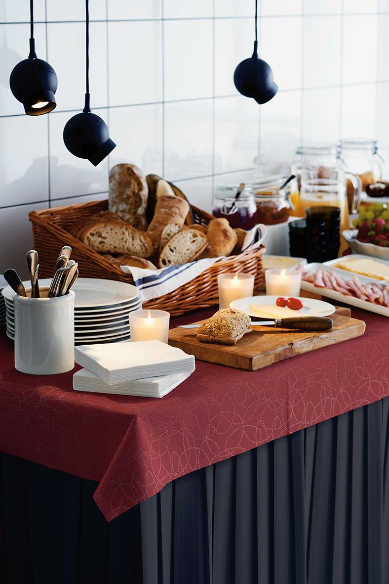 Frukostbord med bröd, smör, sylt, koppar, ljus och duk i kök med vita kakelväggar och svarta lampor