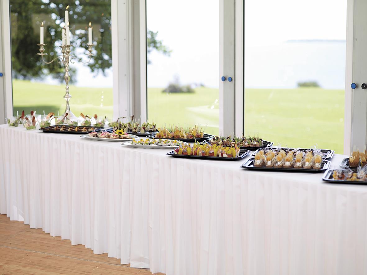 Vit dukjol Duni Dunicel 0,72x4m på buffébord med mat och dekorationer framför stora fönster med utsikt över grönt landskap