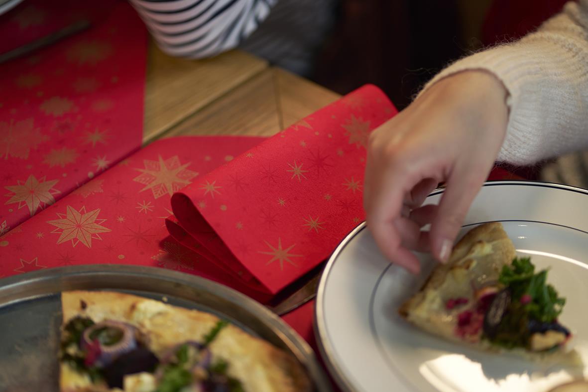 Person som tar en bit av en paj eller tårta på en tallrik med juldekorationer och servetter i bakgrunden